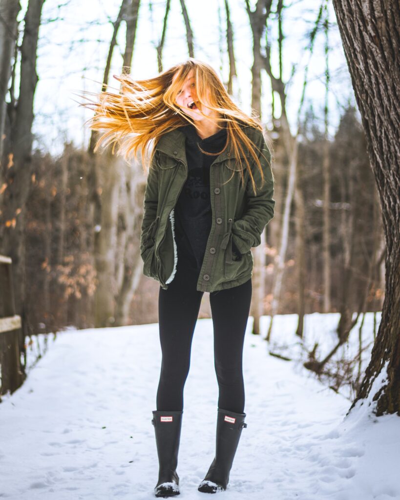 A woman standing between trees wearing Hunter boots